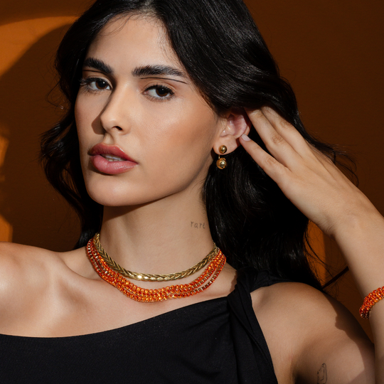 Mulher usando o kit completo riviera laranja com colar, pulseira e brinco bola dourados