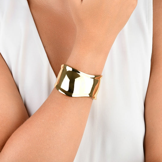 Detalhe do acabamento espelhado e formas fluidas do bracelete liso dourado