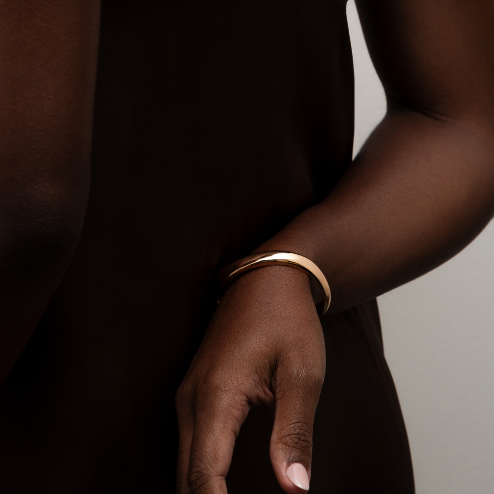 Bracelete curvas dourado usado no pulso em composição elegante
