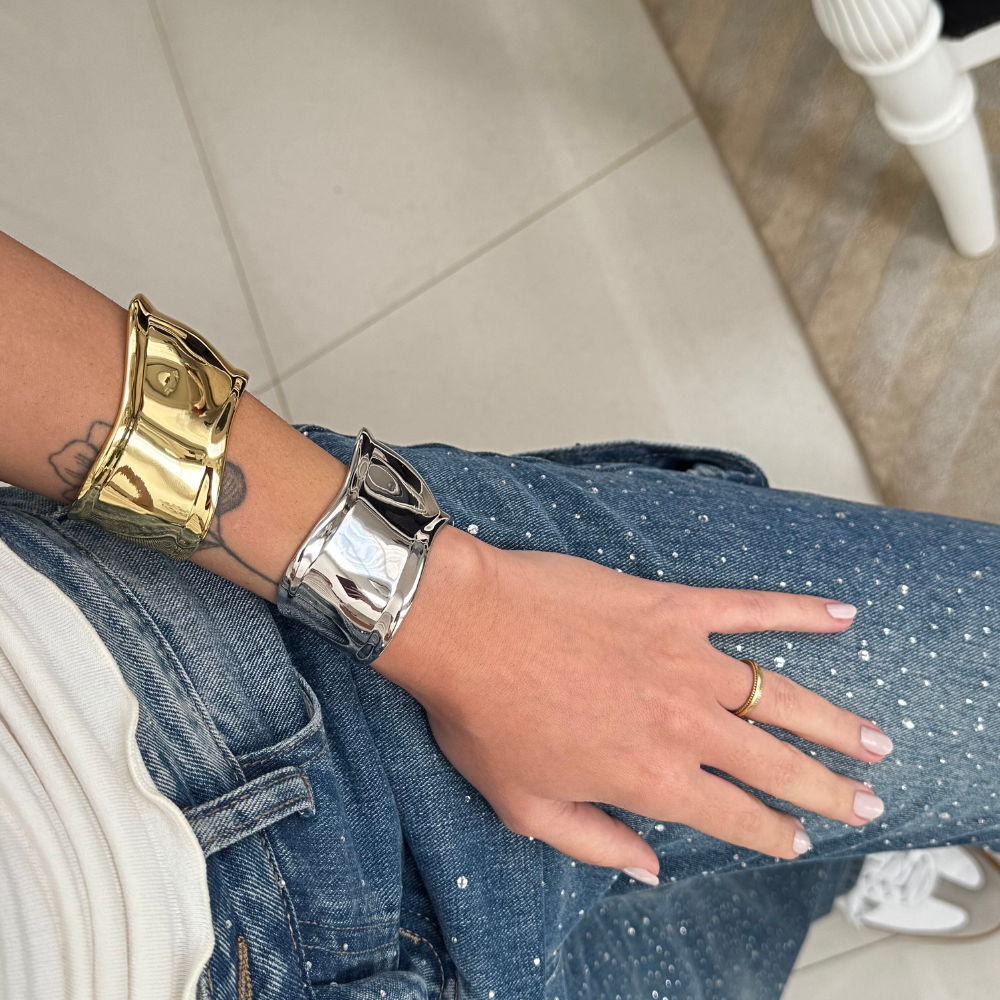 Mulher usando bracelete liso dourado no pulso, destacando o brilho e modernidade da peça