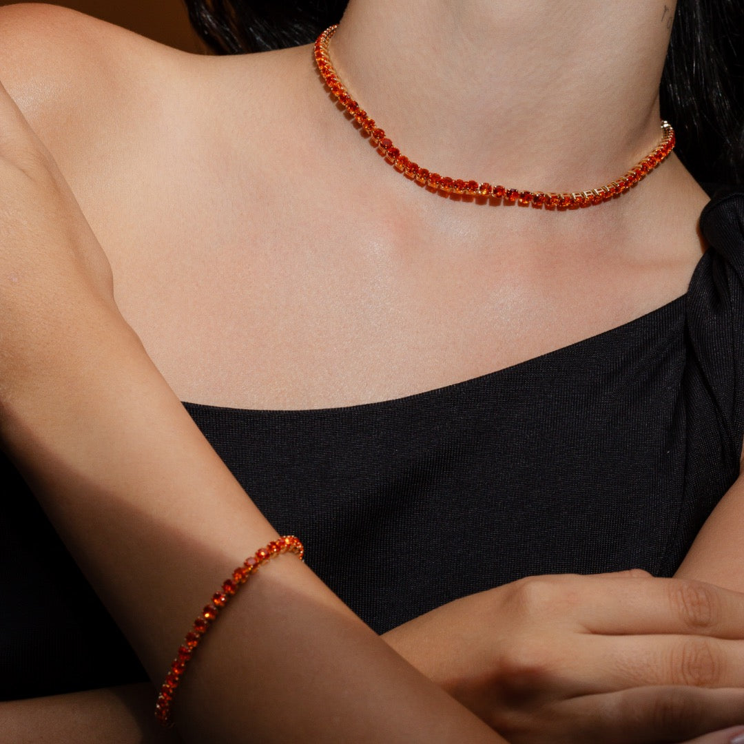 Mulher usando pulseira riviera laranja banho ouro no pulso