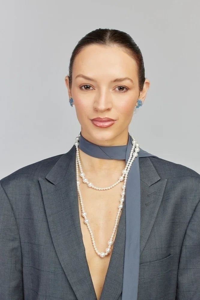 Mulher usando colar de pérolas e brincos azuis com blazer cinza, joias elegantes e sofisticadas